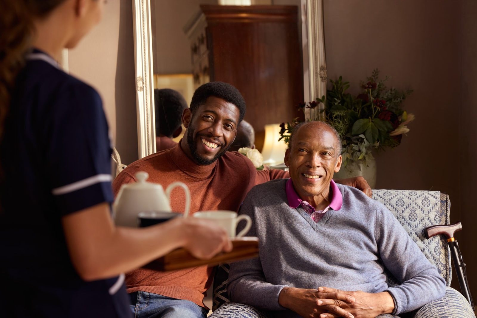 A carer bringing tea to two men on a sofa