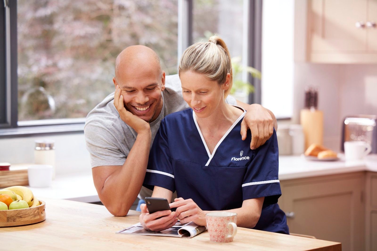 Florence: a nurse and a man laughing over a phone in a kitchen
