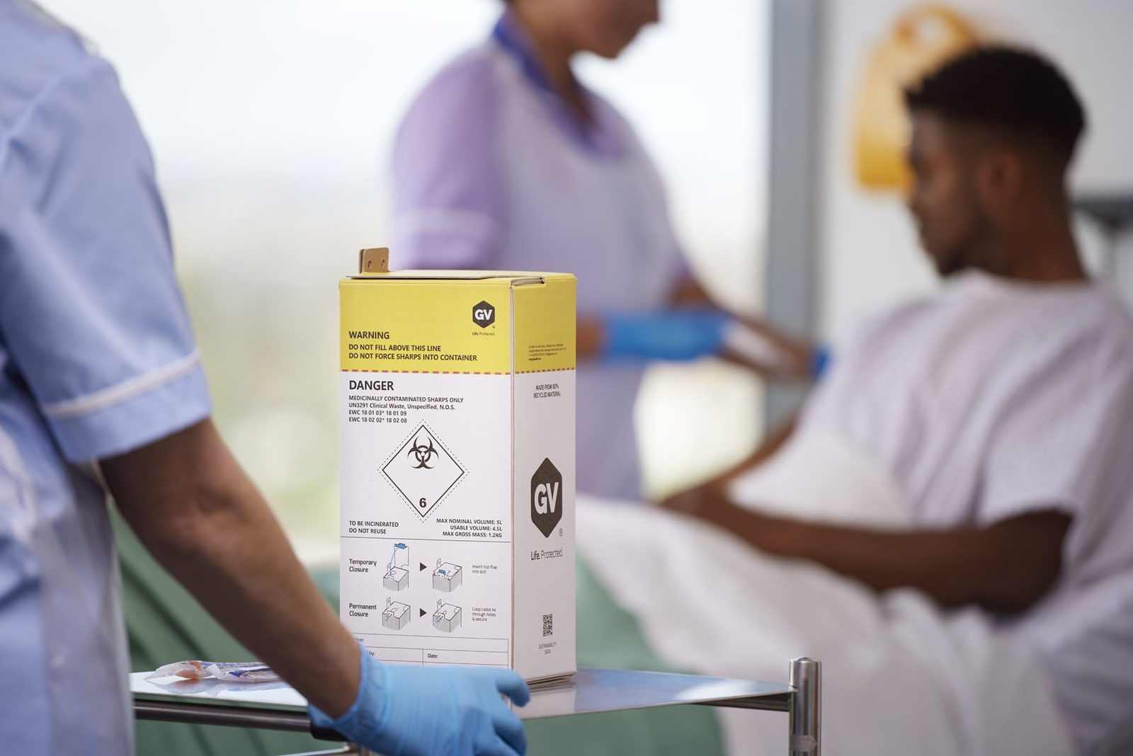 A nurse and a patient on a ward with a sharps box in the foreground