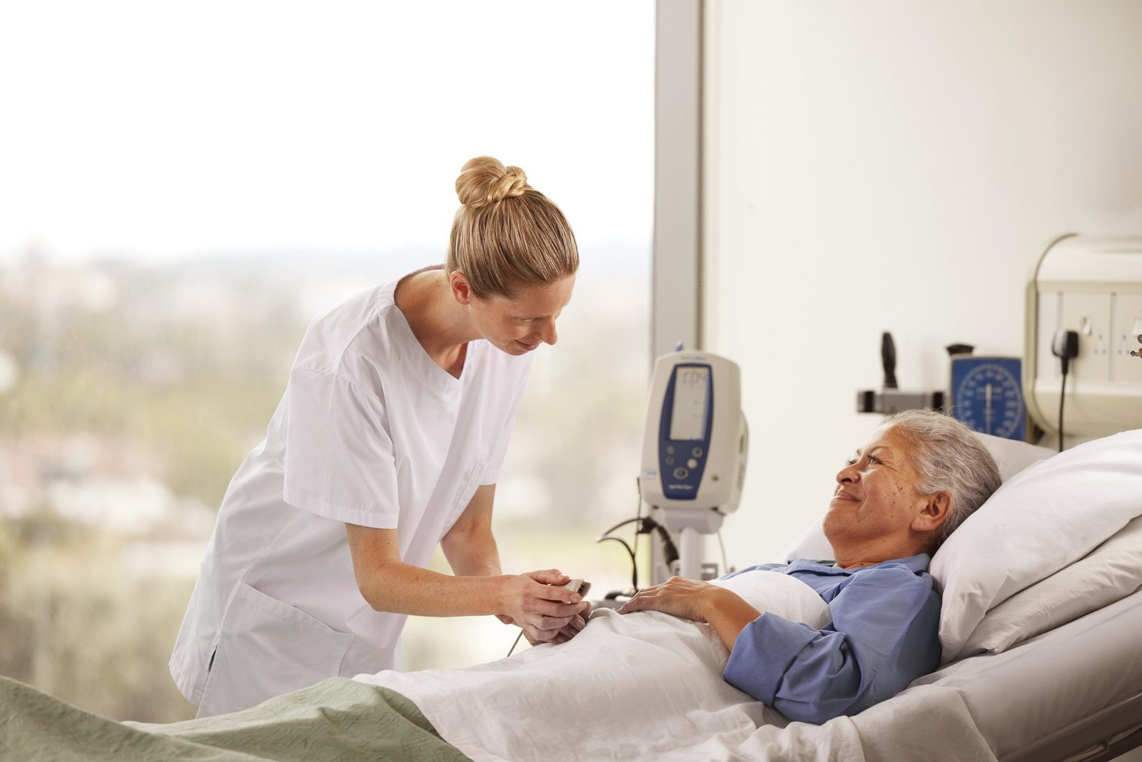 A nurse checking an older patient on a ward, both smiling